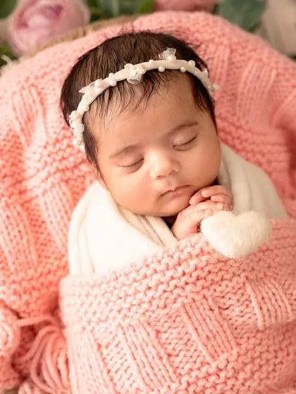 This peaceful portrait captures the baby swaddled and sleeping in a basket, surrounded by a wreath of delicate pink and cream roses.
