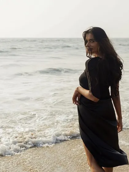 The model walking along the shoreline, showing the movement of the sheer, draped outfit against the waves.