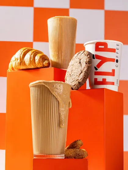 A dynamic composition for Flyp Coffee with multiple products, a checkerboard background, and an overflowing glass, creating a fun and energetic brand image.