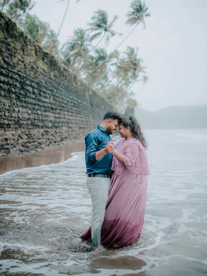 A romantic pose by the sea, with the couple holding hands against a backdrop of palm trees and ancient walls.