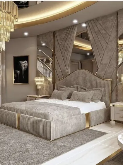 An opulent bedroom featuring a grey upholstered bed with gold trim, mirrored panels, and a dramatic, multi-layered crystal chandelier. The design is perfect for those who love a glamorous aesthetic.