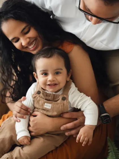 A sweet moment with parents looking down at their smiling baby. This is a lovely, intimate shot from a family photoshoot.