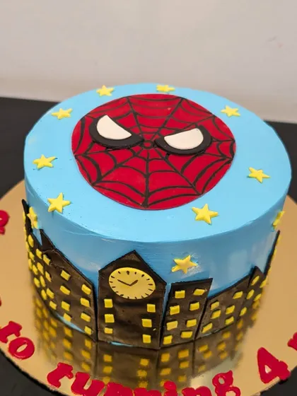 A Spider-Man cake for a 4th birthday celebration. The design features the iconic mask on top of a city skyline that wraps around the cake.