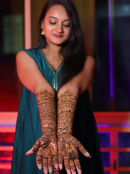 A happy bride showcasing her complete bridal mehndi. The design covers her hands and arms in beautiful, traditional patterns that complement her festive look.