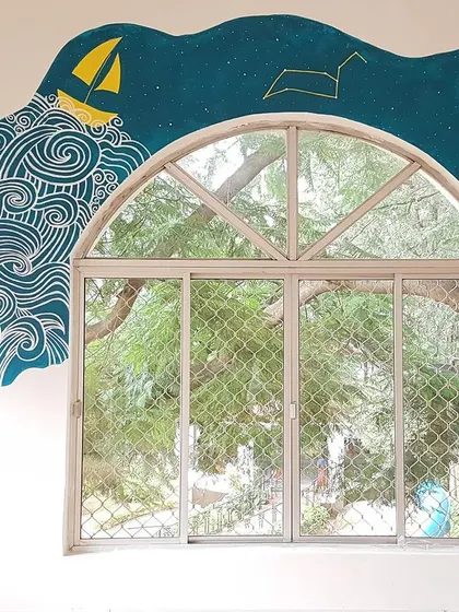This mural was designed around a large arched window in a school. The paint tube appears to be squeezing out an ocean of imagination, perfectly framing the view outside.