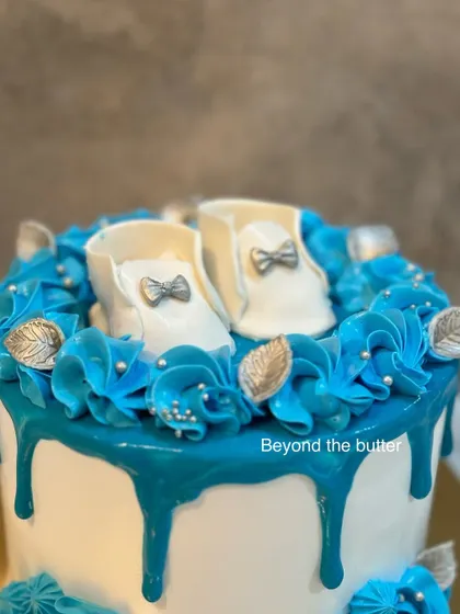 A close up of the adorable, handcrafted fondant baby booties that topped this "Welcome Baby" cake. The intricate details, like the tiny silver bows, make it extra special.