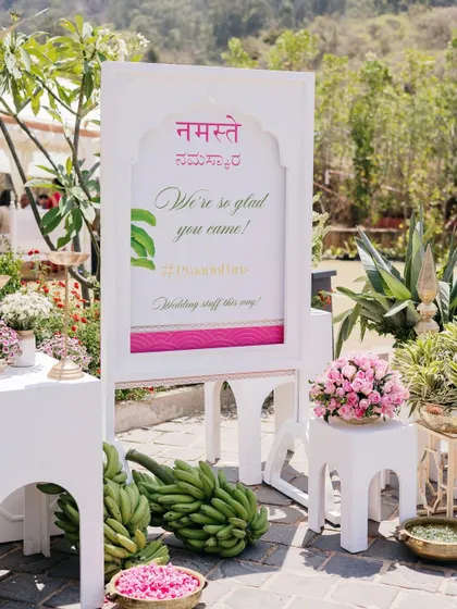 The welcome sign is flanked by fresh flowers and auspicious banana bunches.