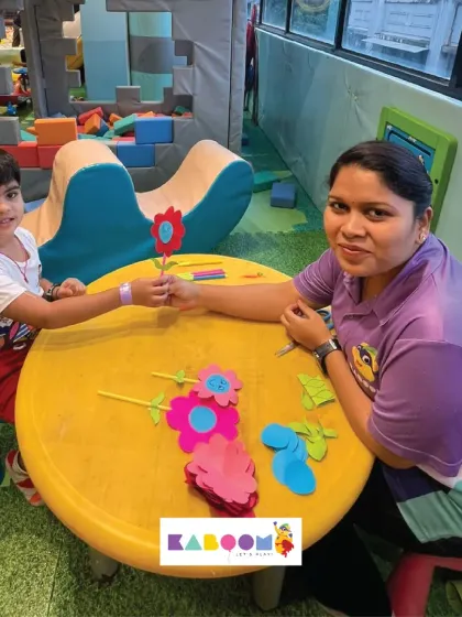 A staff member helps a young boy assemble his paper flower craft. These guided activities are great for developing fine motor skills and following instructions.