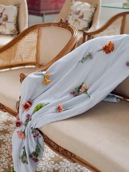 The beauty of handmade details. For this engagement, we hand-stitched individual flowers onto this light blue throw, adding a delicate and personal touch to the classic rattan-weaved seating.