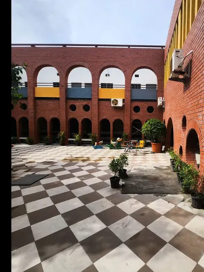 The refurbished internal courtyard of a primary school, featuring a facade of brick arches and a checkered floor. The open, airy space is designed to be a central hub for play and interaction.