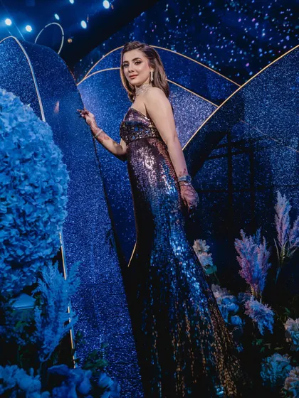 The bride stands amidst the decor, where glittering blue panels and soft, ethereal florals in shades of blue and lavender come together to create a dreamy, celestial photo corner.