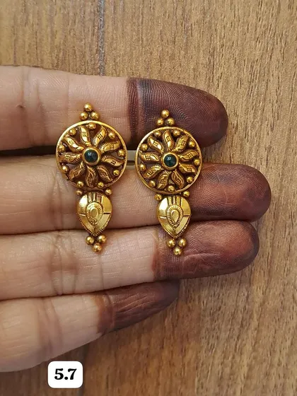 These gold-plated silver earrings feature a beautiful floral or sun-like motif with a dark stone at the center. The antique finish adds to their traditional charm.