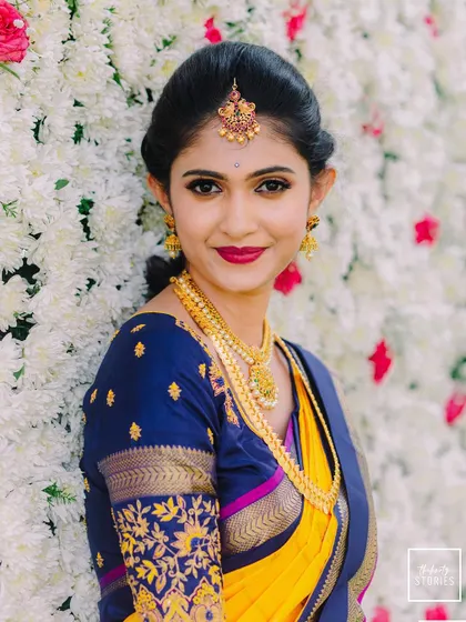 A beautiful close-up of the bride against a wall of white flowers, highlighting her flawless makeup and traditional attire.