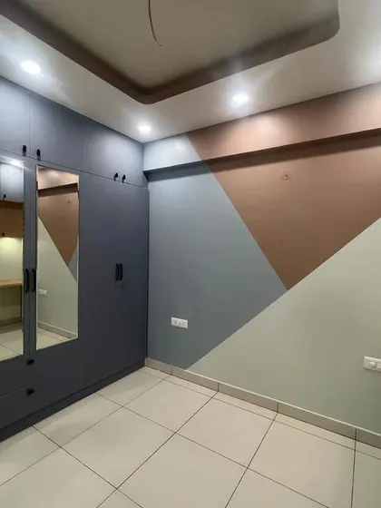 A bedroom in a newly finished project, featuring a grey wardrobe with mirrored doors and a geometric accent wall. This shows the completed fixed furniture and paintwork.