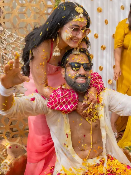 The pure, uninhibited joy of a Haldi ceremony. The couple, covered in turmeric and flower petals, share a playful and happy moment, perfectly capturing the spirit of the celebration.