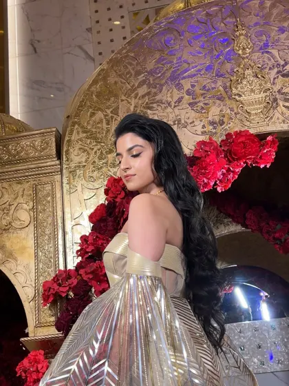 The bride looks like a goddess in her metallic gown, with her hair styled in long, flowing waves that add to the drama of the look.