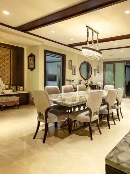 This image shows a cohesive design where a formal dining area, centered around a heavy marble-topped table, coexists with a dedicated prayer nook. The consistent use of dark wood and traditional patterns creates a unified and harmonious environment.