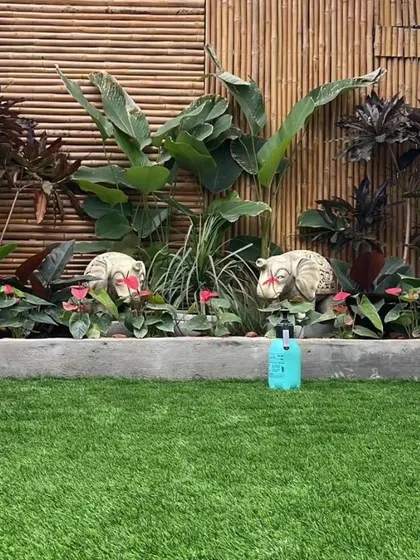 A playful and green backyard design. We used high-quality artificial grass for a maintenance-free lawn and created a raised planter bed with a bamboo backdrop, filled with a mix of tropical foliage and decorative statues.