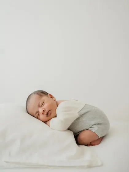 Curled up and dreaming on a soft white pillow. This pose mimics how they sleep in the womb and is a classic for newborn photography.