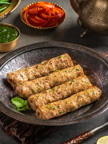 Mutton Gilafi Seekh Kebab, coated with herbs and spices, served on a traditional metal plate.