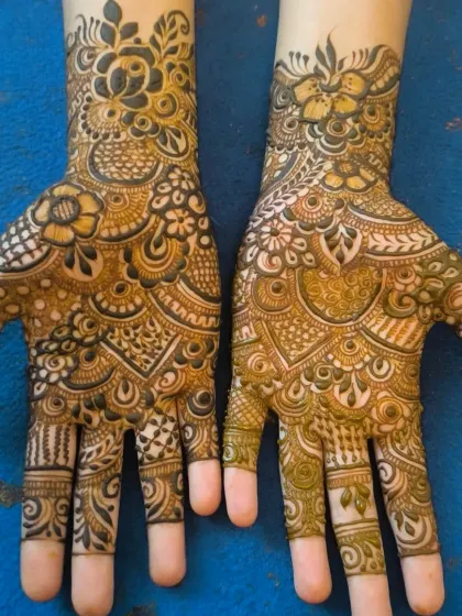 A close-up of a Bombay-style henna design on the hands. Notice the fine lines and the mix of bold flowers with delicate, net-like fillers.