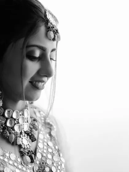A moment of quiet joy captured in classic black and white. This portrait highlights the bride's beautiful smile and the intricate details of her mirror-work jewelry, creating a timeless and artistic image.