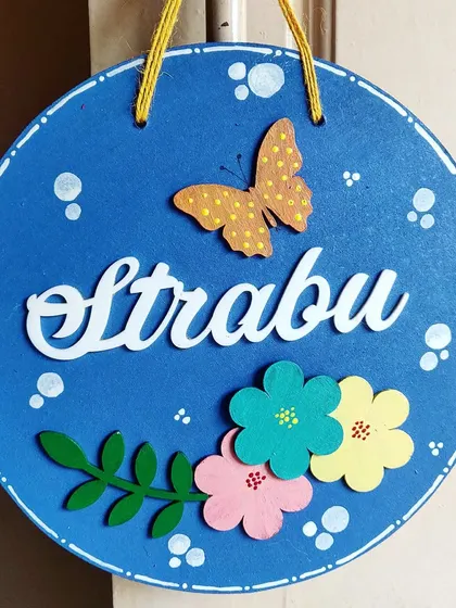 A simple yet beautiful nameplate design featuring a butterfly and colorful flowers. The bright blue base makes the white acrylic name and floral elements pop, creating a fresh and inviting look.