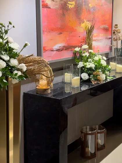 A console table styled with a mix of tall gold vases, candles, and smaller arrangements, all complementing the abstract art on the wall.