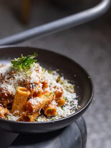 A generous blanket of freshly grated parmesan cheese covers this bowl of Rigatoni Arrabbiata. It's the perfect finishing touch for a classic, spicy pasta dish.