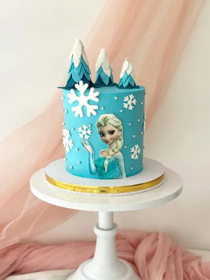 Let it go with this Frozen-themed cake. It features an edible image of Elsa against a snowy blue background, with fondant snowflakes and frosted trees on top.