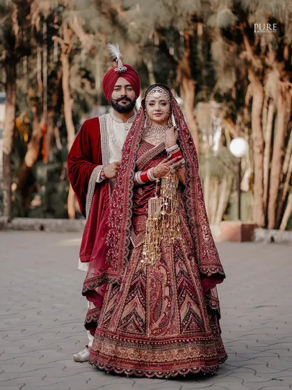 A classic wedding portrait where the bride and groom stand together, showcasing their magnificent wedding attire and the bride's beautiful kaleere.