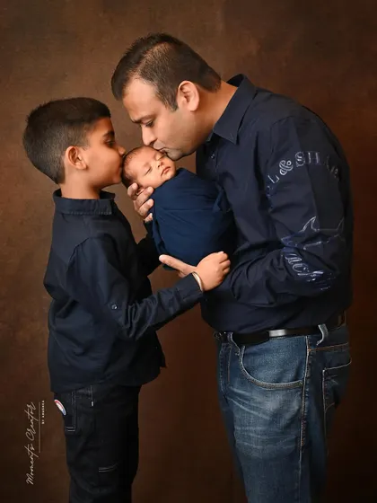A touching moment between a father, son, and the new baby. The gentle kisses from both dad and big brother show the immense love for the family's tiniest member.