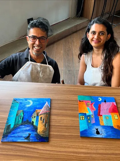 A couple proudly displaying their finished puzzle paintings. Each one tells a different story, with vibrant colors and whimsical scenes.