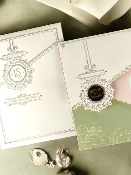 This alternate view of the cream and sage green invitation highlights the intricate monogram and the unique, layered construction.