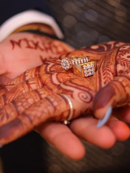 A detailed shot of the engagement rings held in hands adorned with mehndi. This photo beautifully connects the pre-wedding traditions with the engagement ceremony.