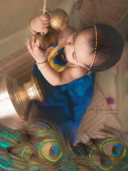 An artistic top-down shot of a baby styled as Radha, reaching for traditional brass bells. This creative angle adds a unique perspective to the mythological theme.