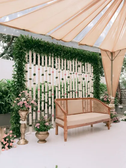 For an intimate and earthy engagement, I chose this elegant cane sofa. The backdrop is a screen of hanging tuberose garlands, framed by lush greenery, creating a look that is both minimalist and traditionally inspired.