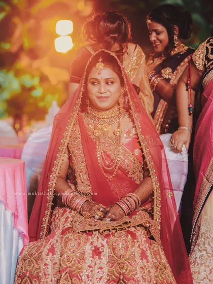 A beautiful portrait of the bride, seated and glowing in her stunning red and gold lehenga, taking in the moments of her special day.