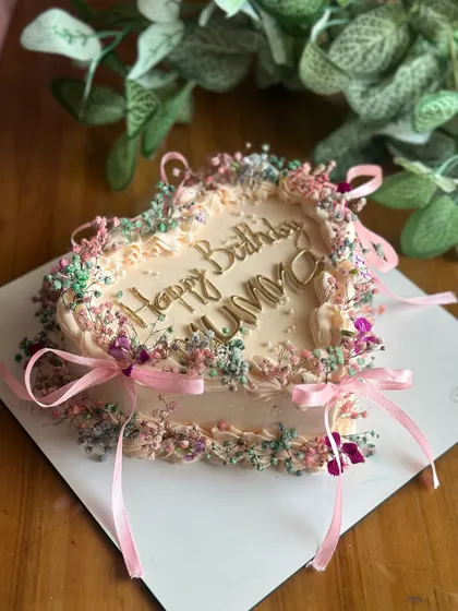 A cake straight out of a vintage dream. This heart-shaped creation is delicately adorned with baby's breath and tiny ribbons, perfect for a romantic and elegant birthday.
