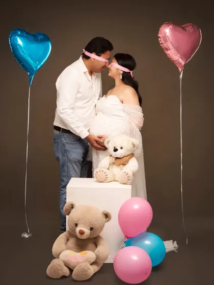A playful and sweet gender reveal concept. The blindfolded couple, surrounded by pink and blue balloons and teddy bears, builds anticipation for the big surprise.
