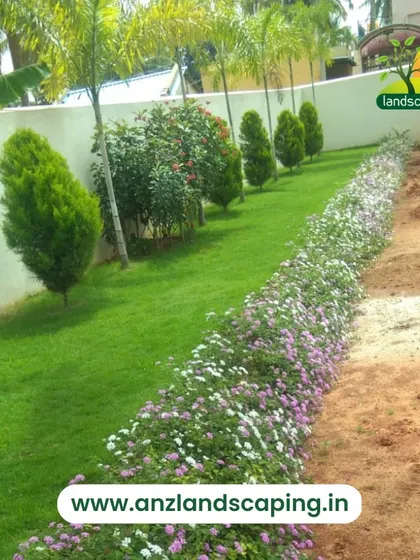 A long garden bed filled with flowering ground cover plants runs alongside a lush lawn, creating a beautiful and colorful border.