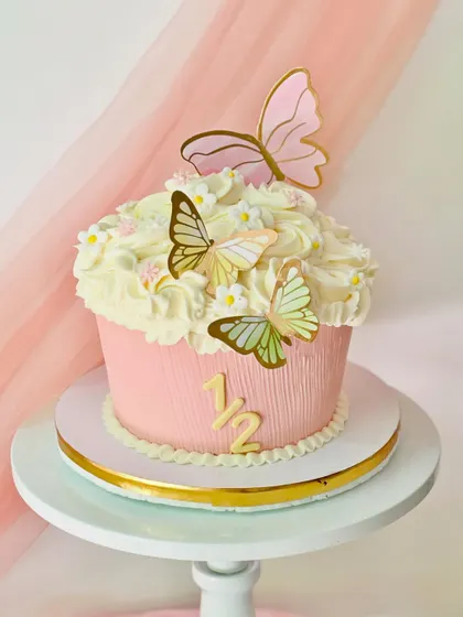 A giant cupcake cake for a half-birthday celebration. This pink cake is decorated with buttercream frosting and delicate paper butterflies.