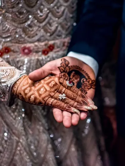 A unique detail shot showing the bride's hand, with its intricate mehndi, resting in the groom's hand, which also features a portrait of his bride in henna.