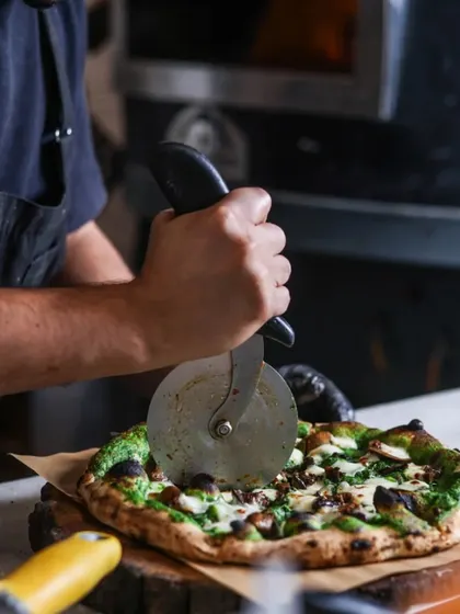 Slicing into a Fungi pizza with a green pesto base. The steam rising from the fresh-cut slice shows just how hot and fresh my pizzas are when they reach you.