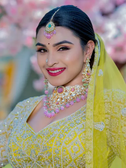 A smiling portrait of the bride, showcasing the complete look with the maang tikka, necklace, and earrings. The bright colors radiate pure happiness.