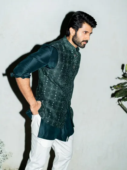 Vijay Deverakonda in a layered look by Divyam Mehta. The printed waistcoat over a dark teal kurta, paired with white trousers, is a fresh and stylish combination for festive events.