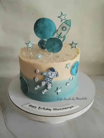 A space themed cake in cool hues of blue. This design features an astronaut floating among planets and stars, perfect for a budding space explorer.
