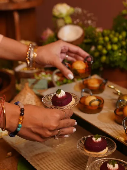 A guest selecting a beautifully crafted beetroot appetizer from a platter. This bite-sized dessert is placed on a delicate glass stand, highlighting the elegance and artistry of our food presentation.