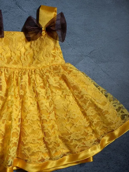 A beautiful yellow lace dress perfect for summer. This close-up highlights the delicate floral pattern of the lace and the contrasting brown organza bows on the shoulders.