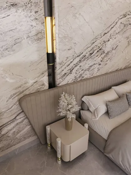 A close-up detail shows the custom bedside table and elegant wall sconce set against the dramatic veining of the marble. Every element is chosen to complement the material palette and enhance the room's luxurious feel.